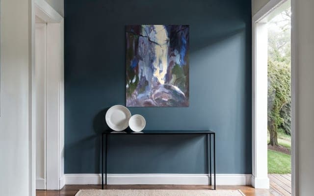 A painting above a console table on a deep-blue hallway wall.